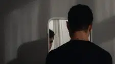 Homem olhando seu reflexo no espelho, ilustrando a transição de mentalidade e a mudança de comportamento na relação com o próprio corpo.